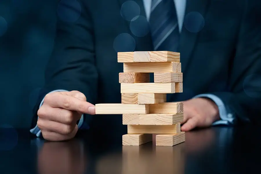A businessman removes a block from a wooden Jenga tower, symbolizing business risk