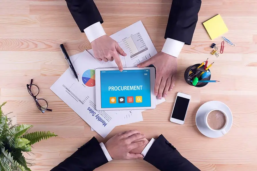 Two people reviewing procurement reports and a tablet showing a procurement app